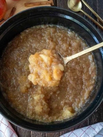 A serving spoon scooping up some applesauce from the slow cooker,
