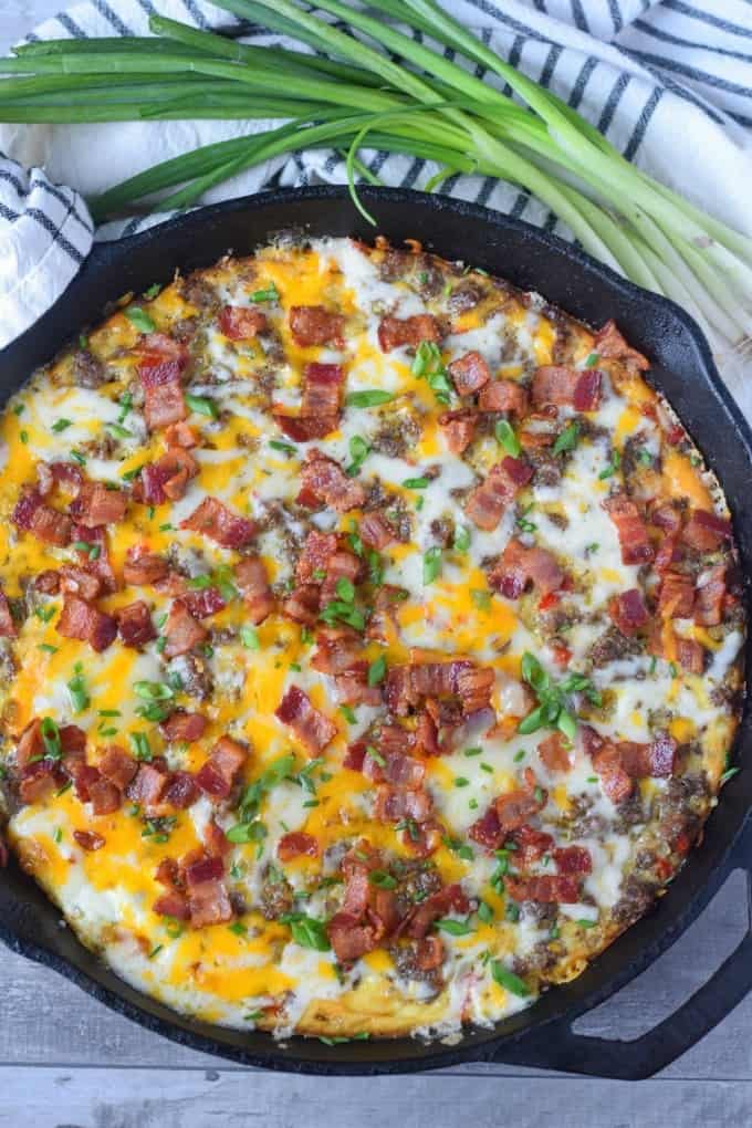 Breakfast casserole in a cast iron skillet with green onions on the side.