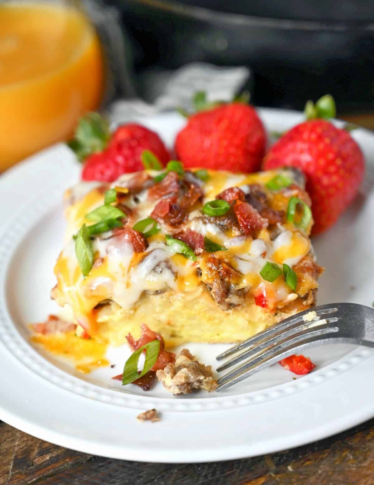 Breakfast casserole on a white plate with strawberries.