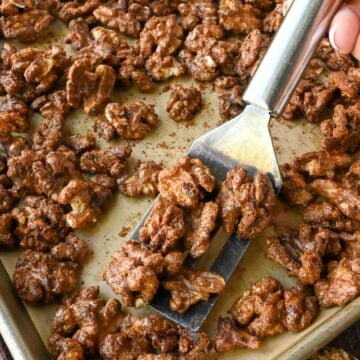 A spatula scooping up some candied walnuts from a baking sheet.