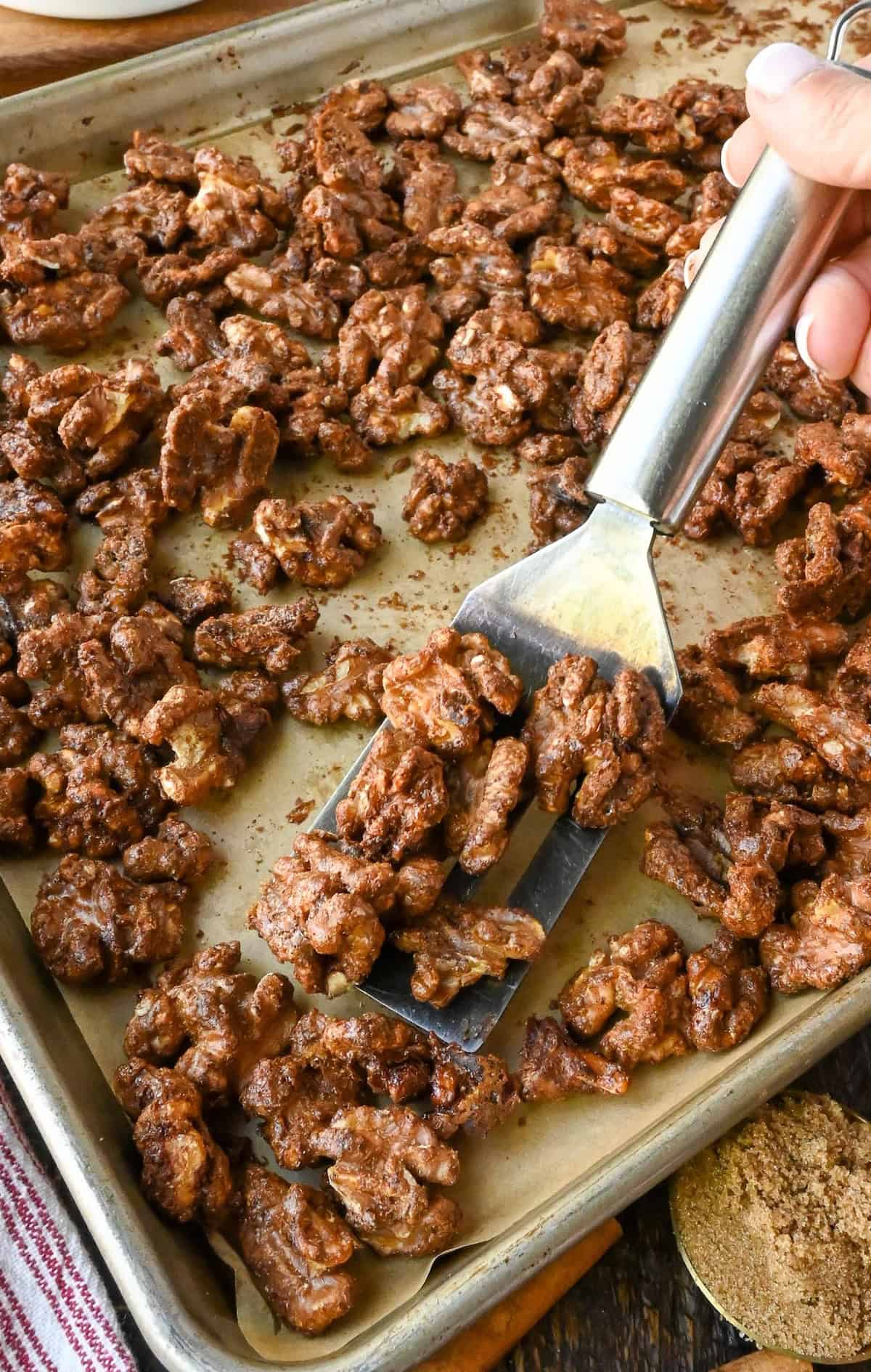 A spatula scooping up some candied walnuts from a baking sheet.