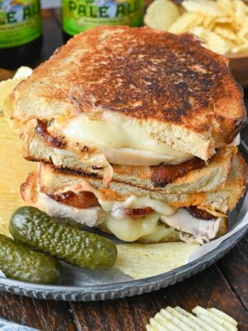 Turkey grilled cheese on a plate with pickles and chips.