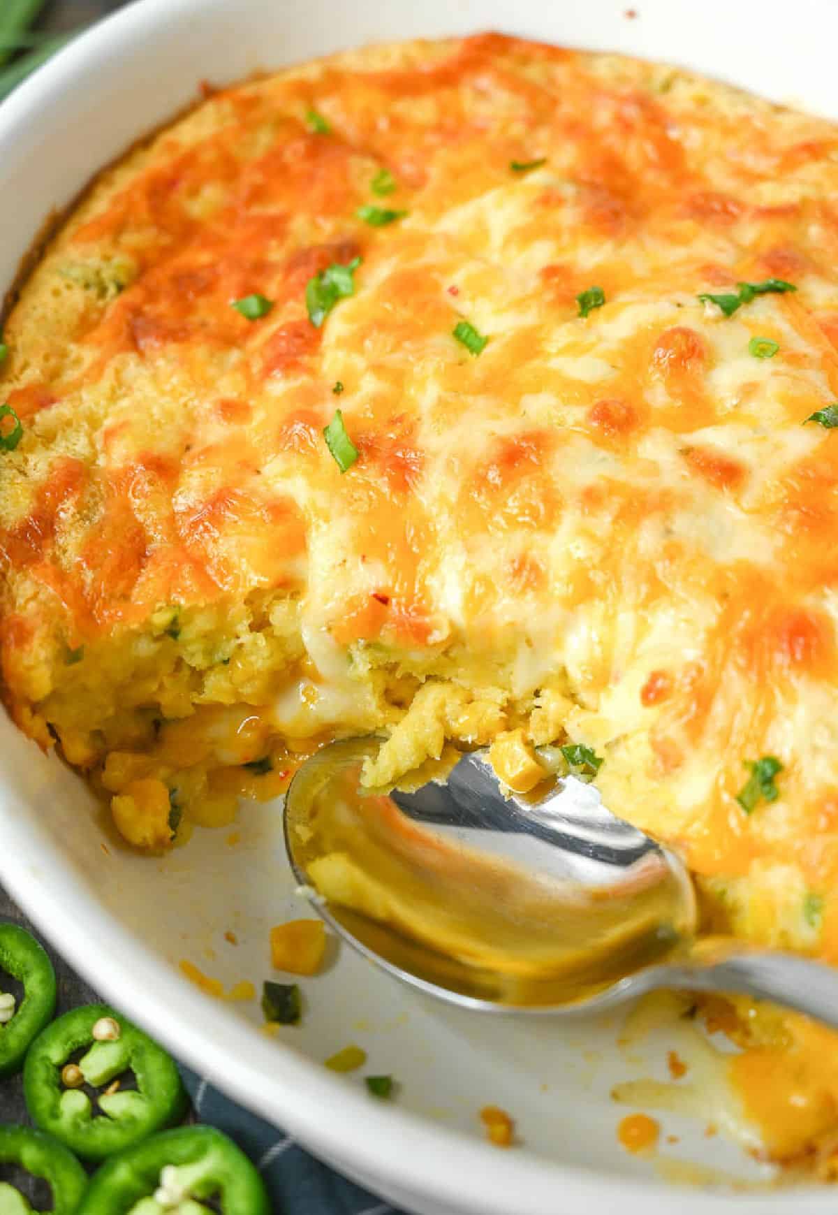 A baking dish with corn casserole in it and a serving missing.