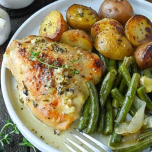 Lemon honey chicken thigh on a white plate with baby potatoes and green beans.