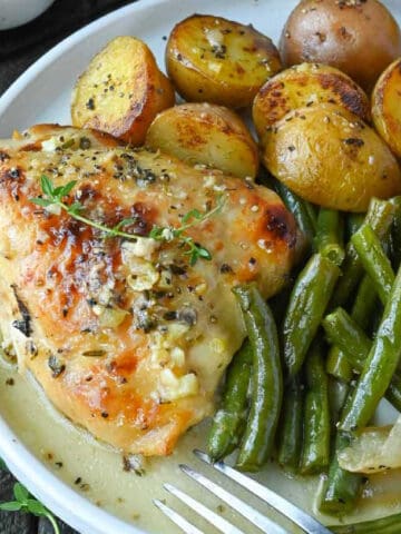 Lemon honey chicken thigh on a white plate with baby potatoes and green beans.