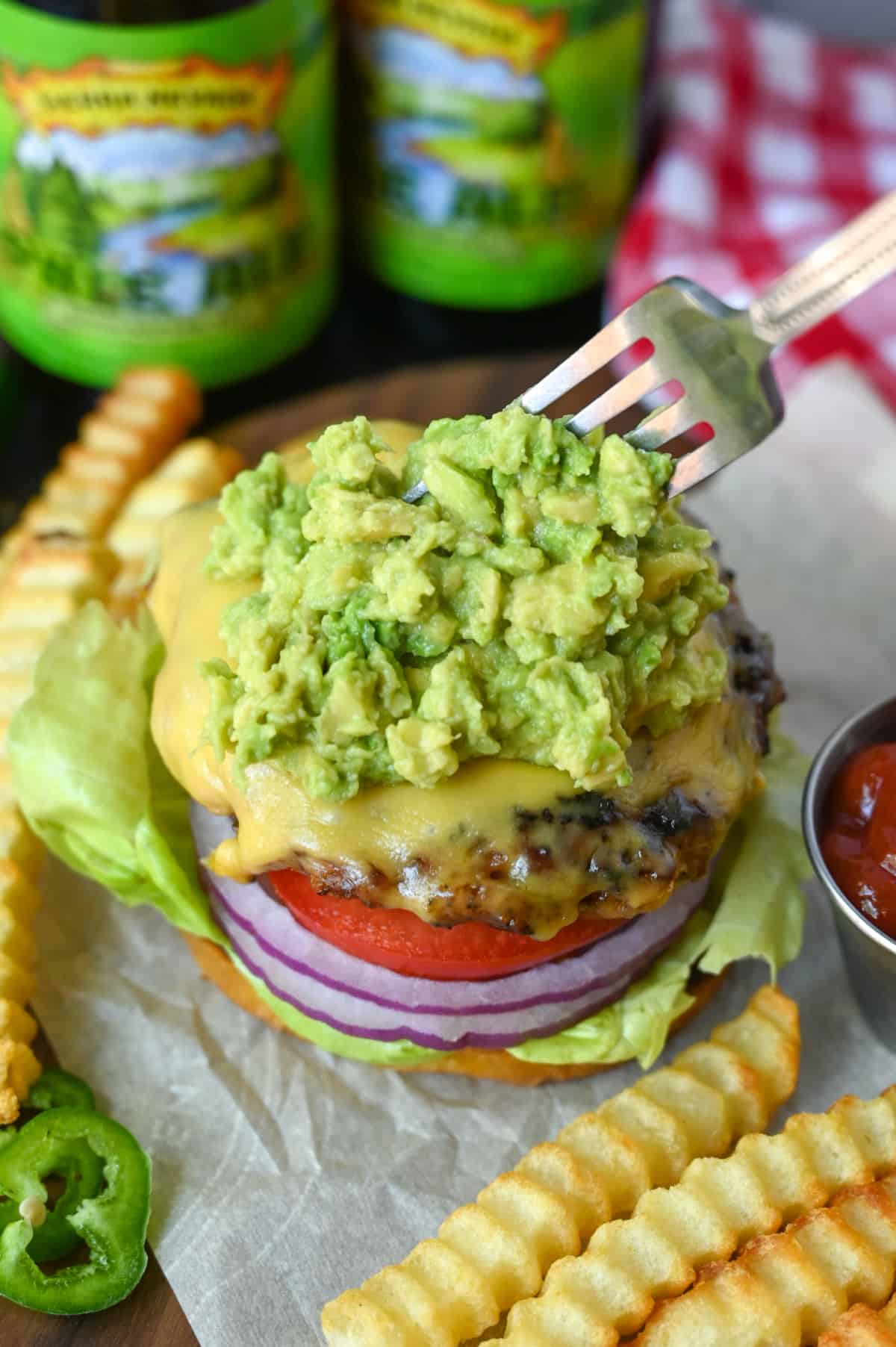 Guacamole being placed on a chicken burger with a fork.