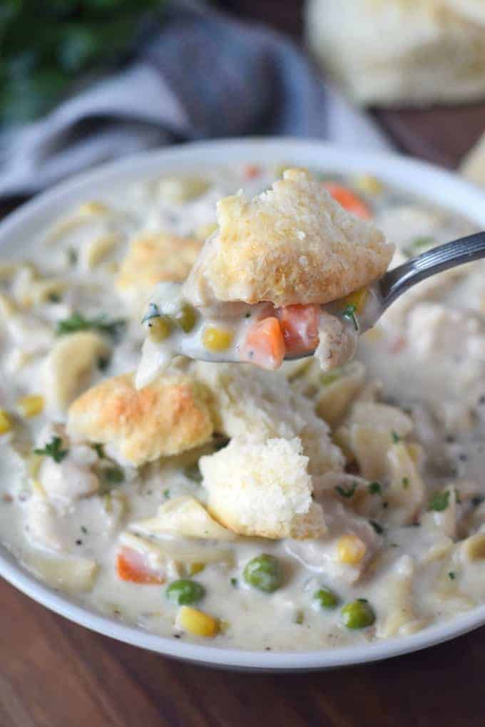 A close up of a bowl of food, with Chicken and biscuits.