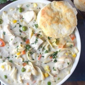 A bowl of chicken pot pie soup with a biscuit.