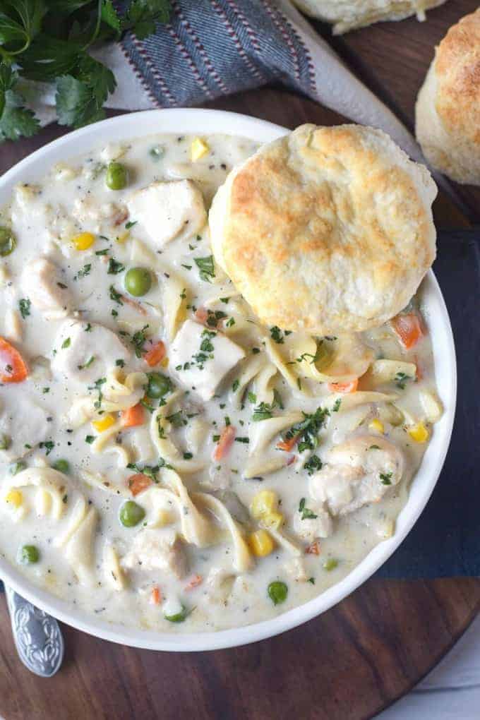 A bowl of chicken pot pie soup with a biscuit.