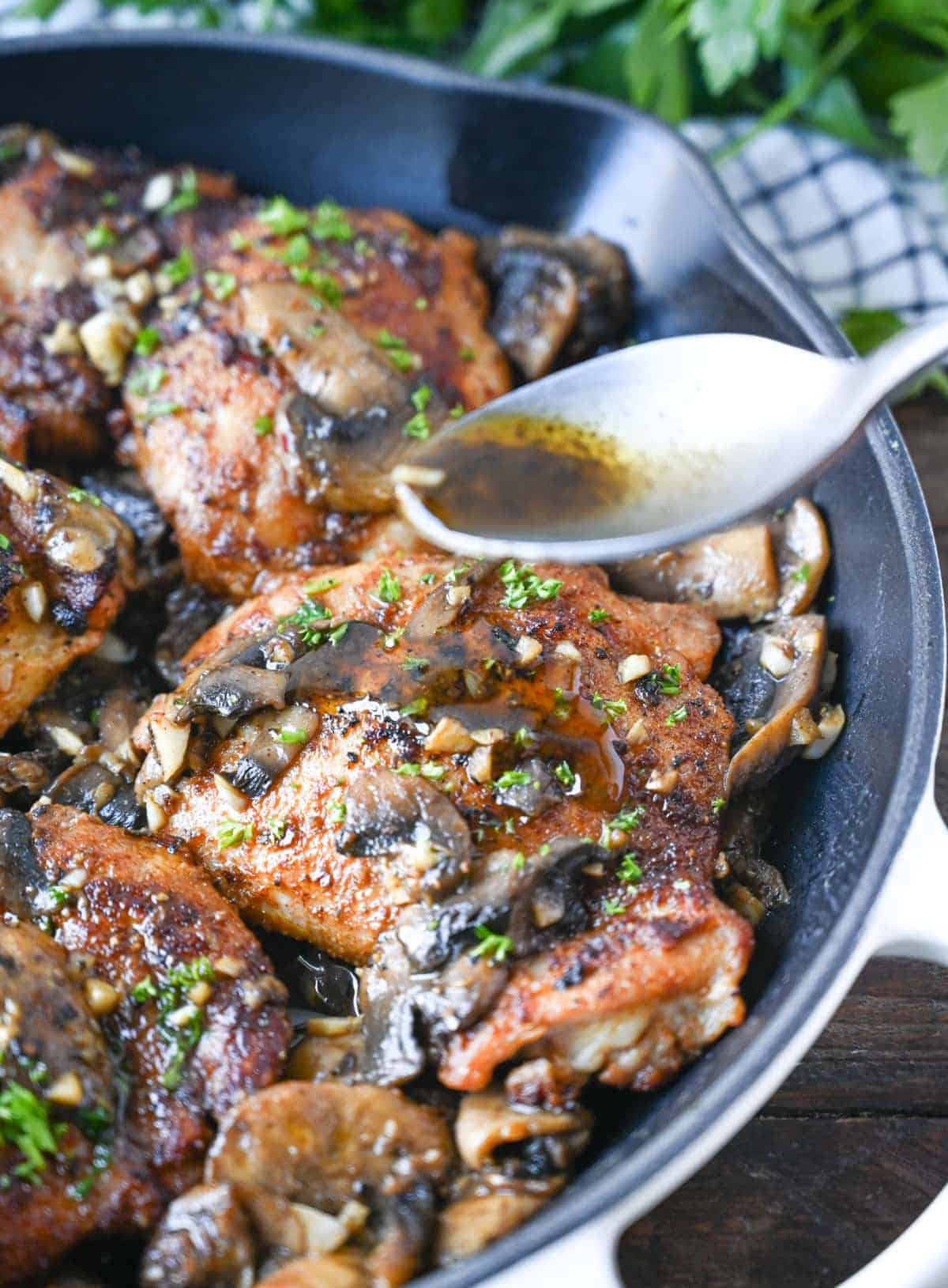 Garlic mushroom chicken thighs in a cast iron skillet with a spoon pouring the juices on top.