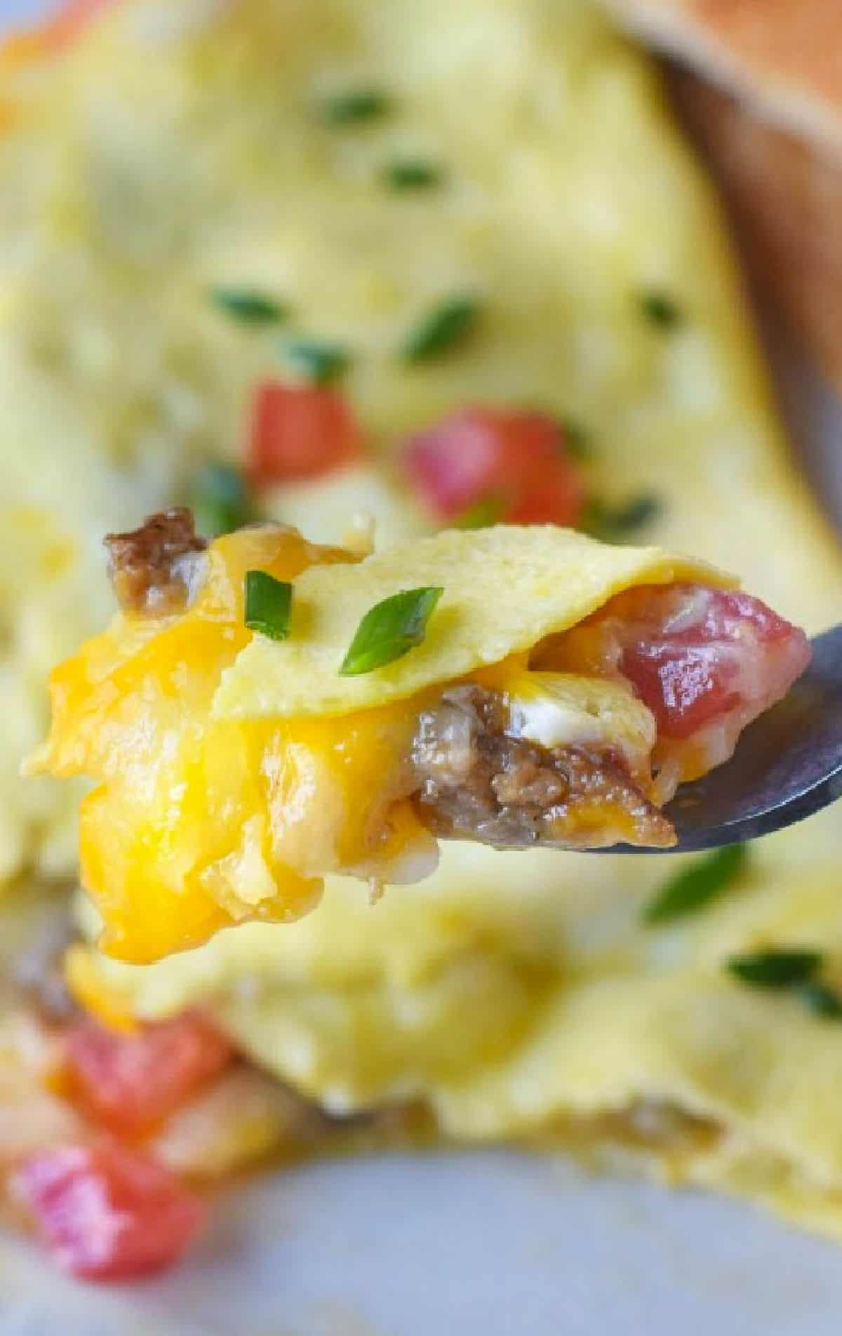 A bite of a sausage omelet on a fork.