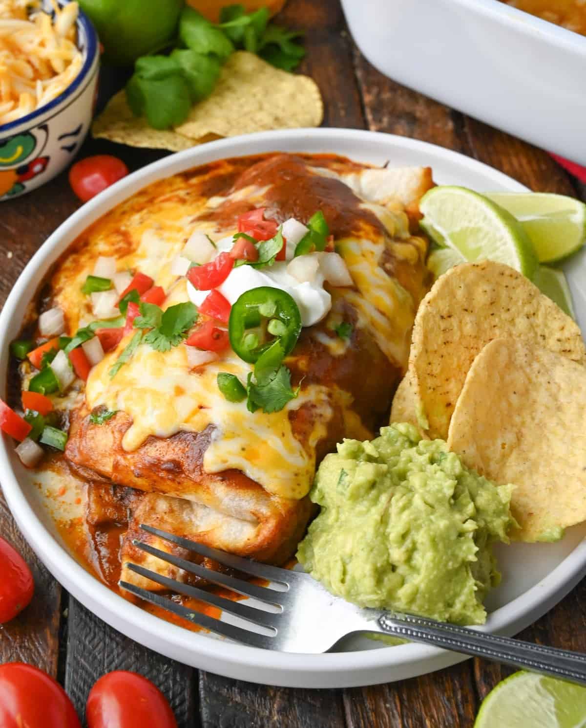 Smothered chicken burrito on a plate with chips and guacamole.