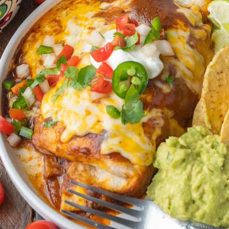 Smothered chicken burrito on a plate with chips and guacamole.