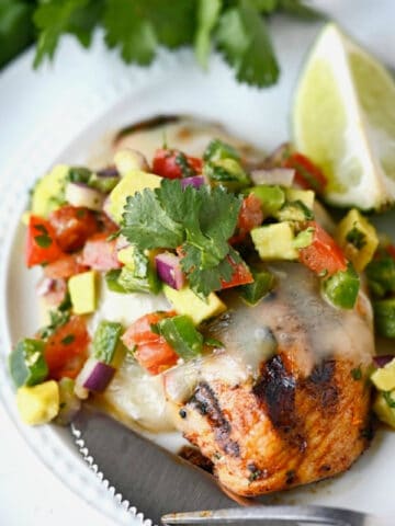 Grilled chicken on a white plate with avocado salsa on top.