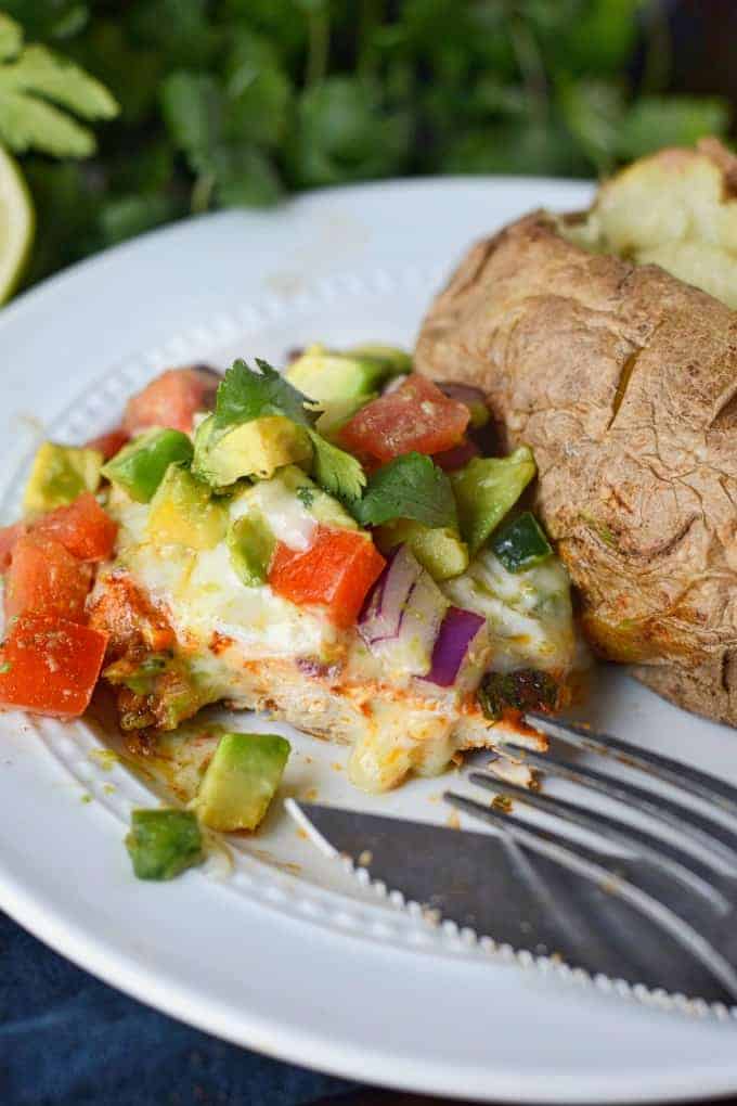 Grilled chicken on a white plate with avocado salsa on top and a baked potato on the side.