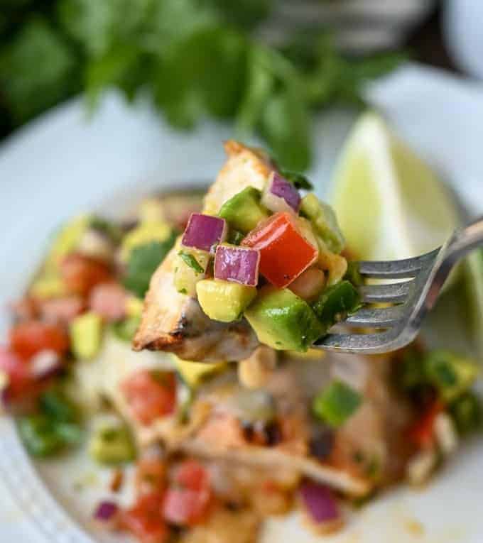 A fork picking up a bite of grilled chicken with avocado salsa on top.