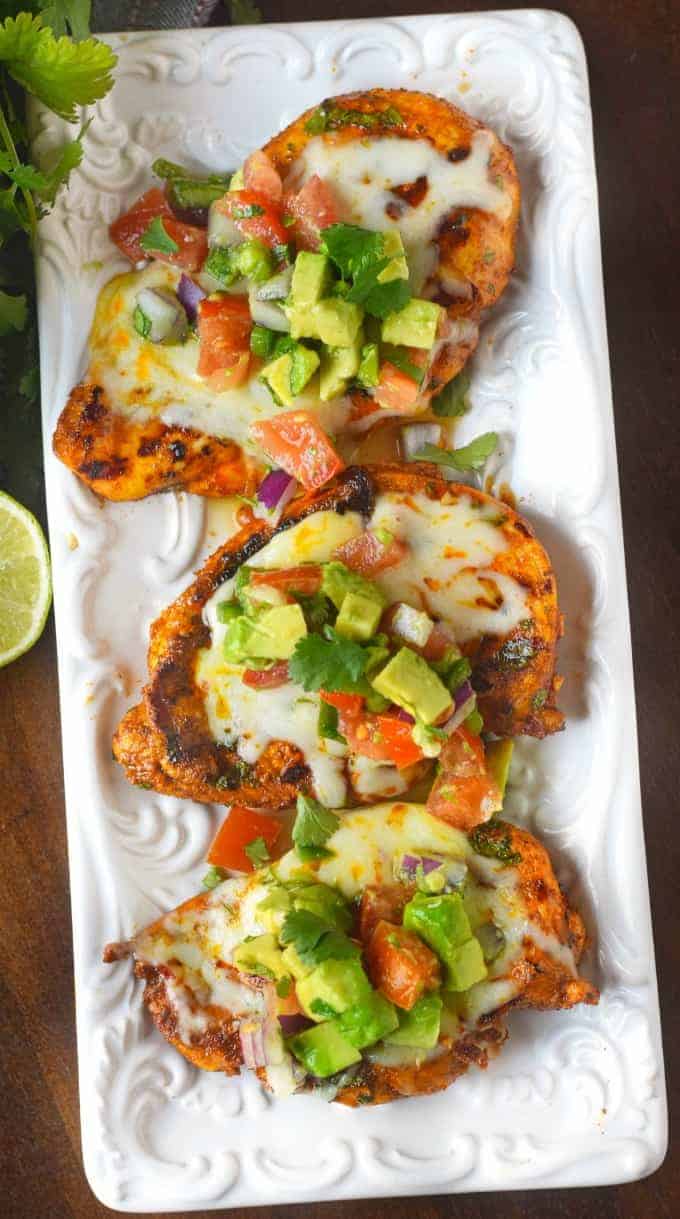 Three grilled chicken breasts on a whilt platter with avocado salsa on top of each one.