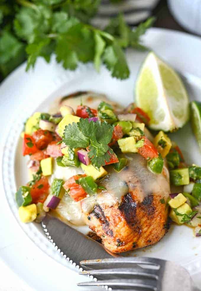 Grilled chicken breasts on a white plate with avocado salsa on top.