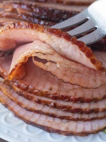 Sliced ham on a white plate and a fork picking up a slice.