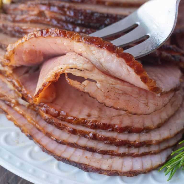 Sliced ham on a white plate and a fork picking up a slice.