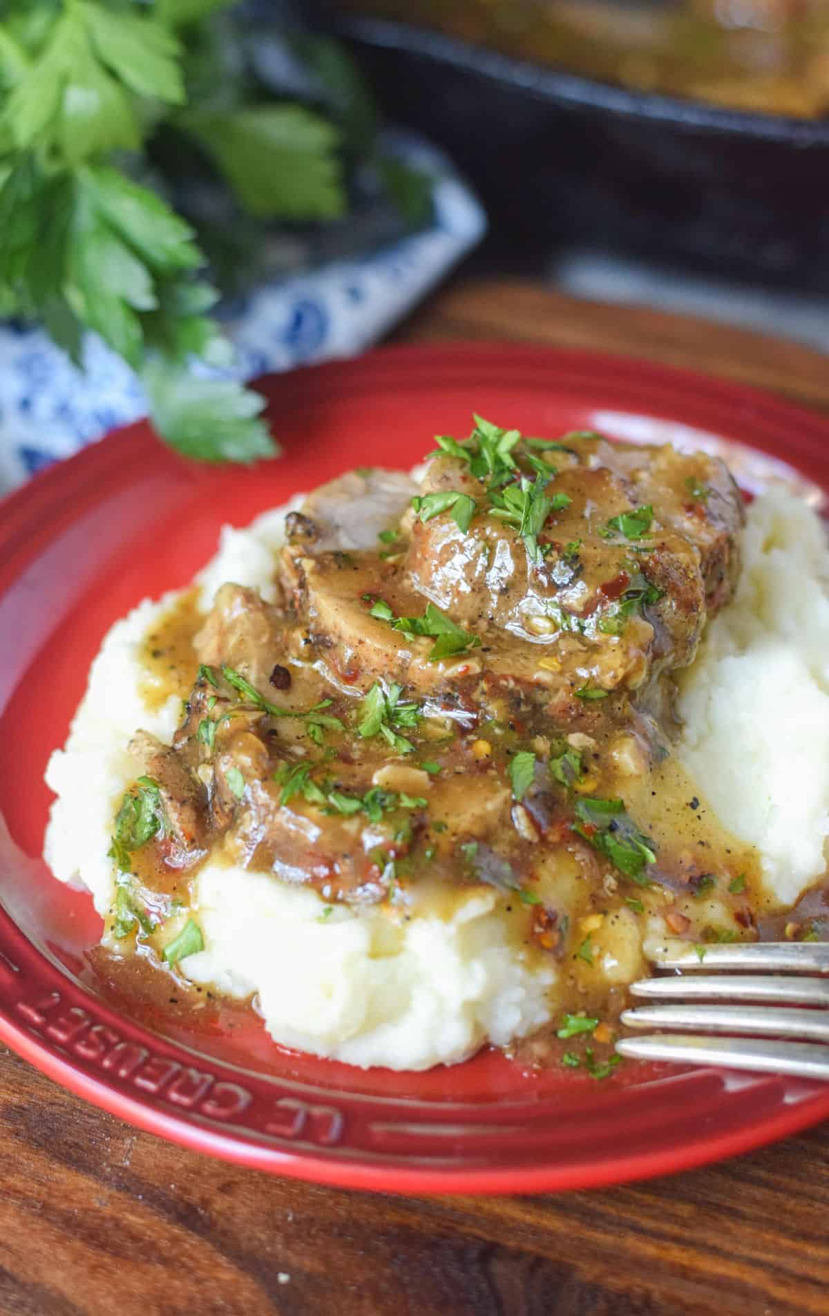 Sliced pork with gravy on top of mashed potatoes.