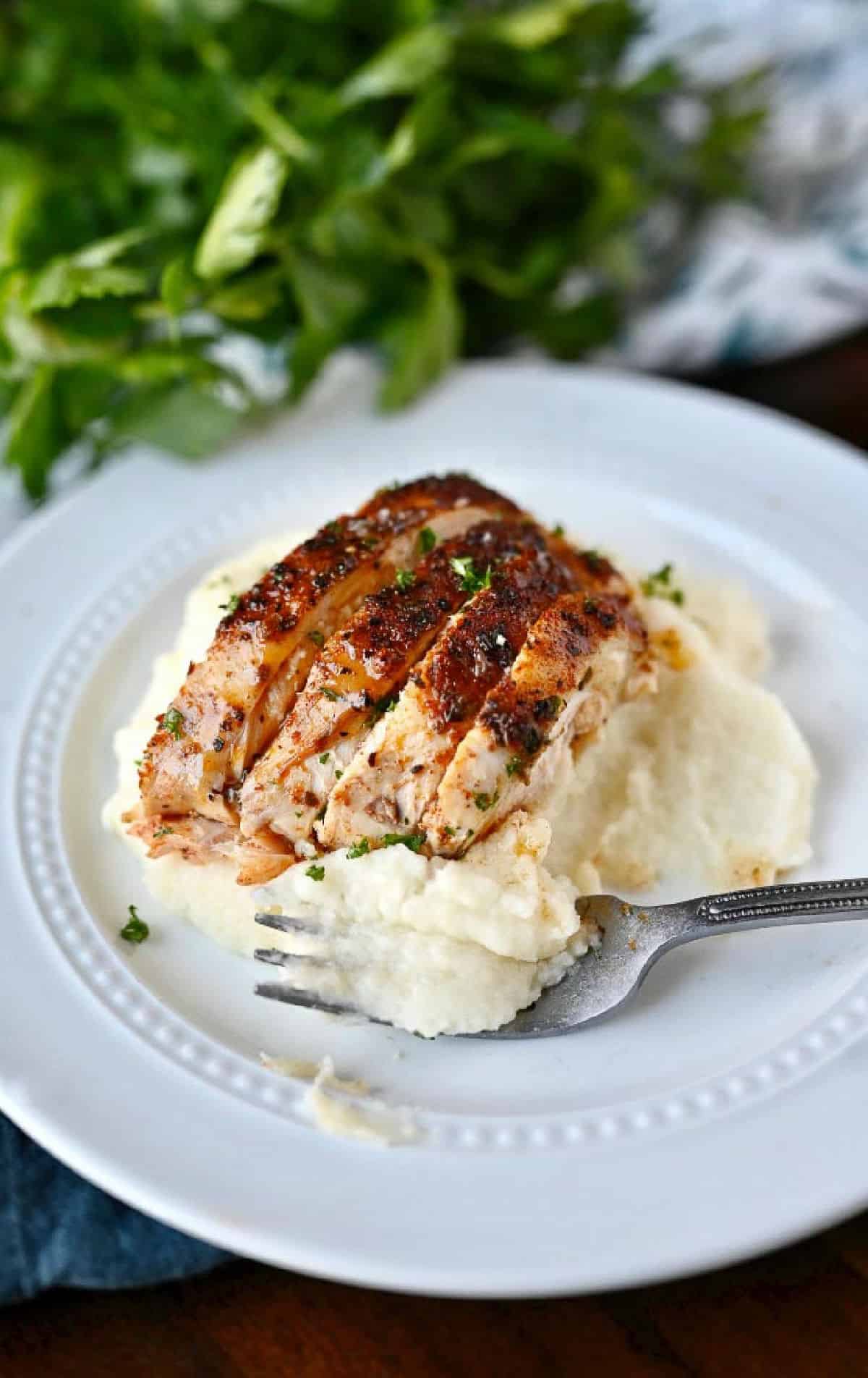 Slices of chicken on top of mashed potatoes.