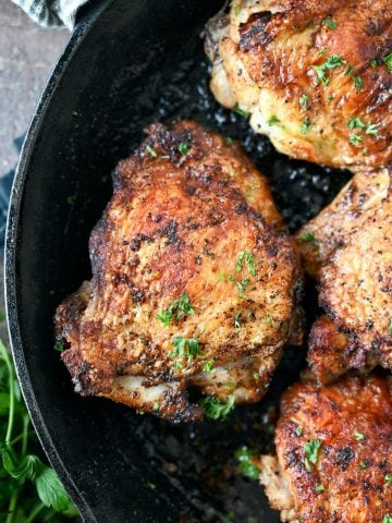 Close up photo of a chicken thigh in a cast iron skillet.