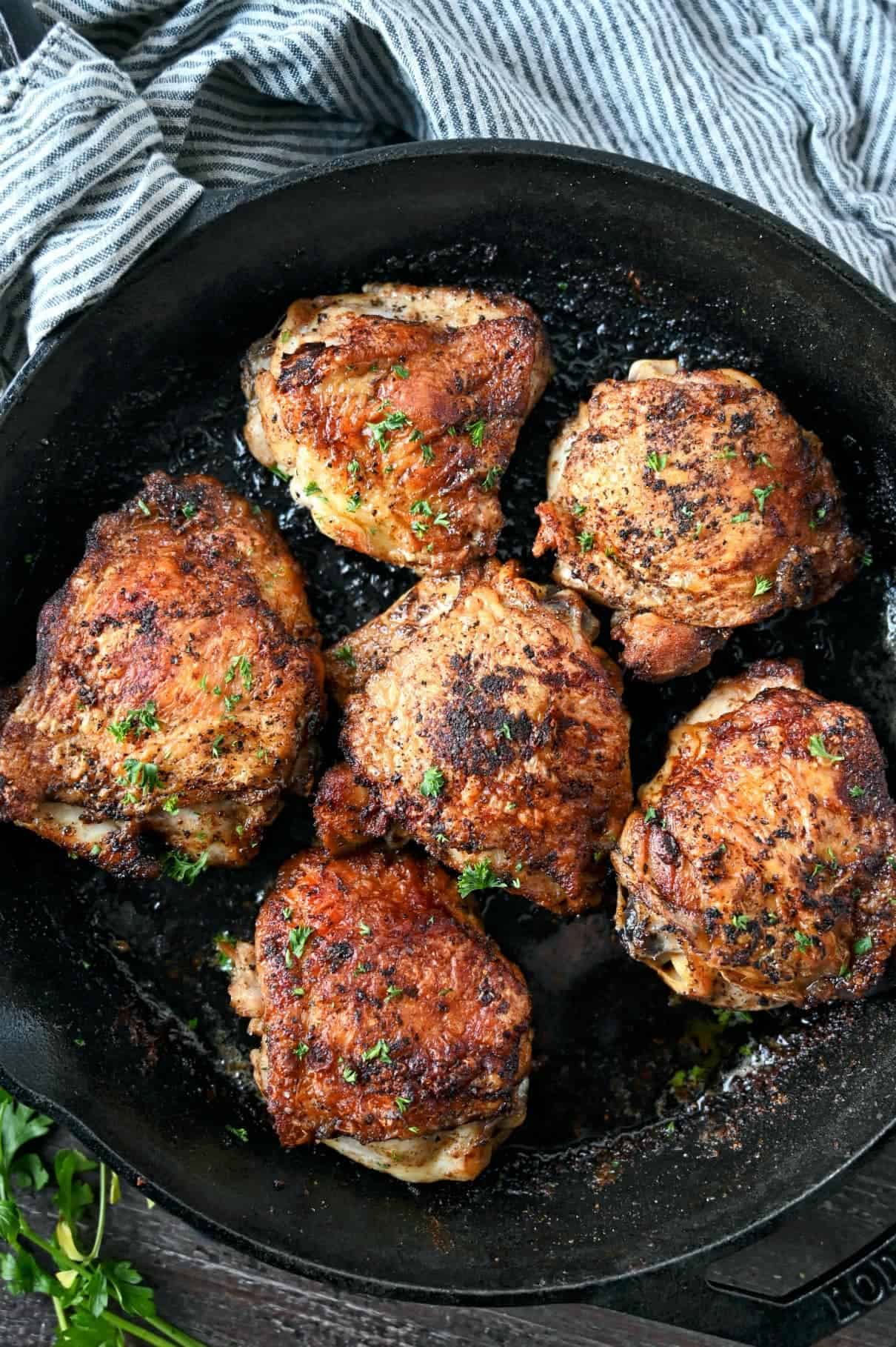 Six chicken thighs in a cast iron skillet.