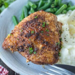 Crispy chicken thigh on a plate with mashed potatoes and green beans.