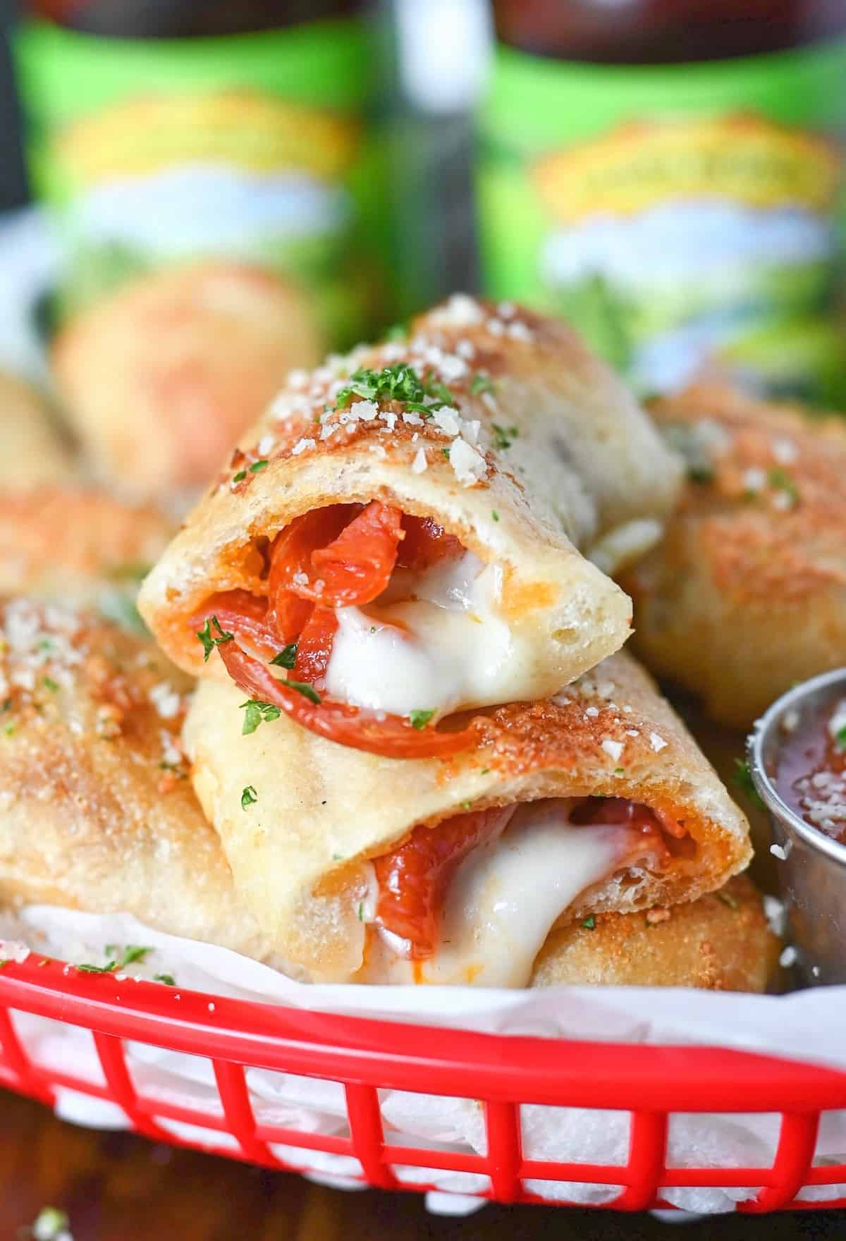 Pepperoni and cheese stuffed breadstick cut in half. Placed in a red basket with cheese oozing out, beer in the background and a side of pizza sauce. 
