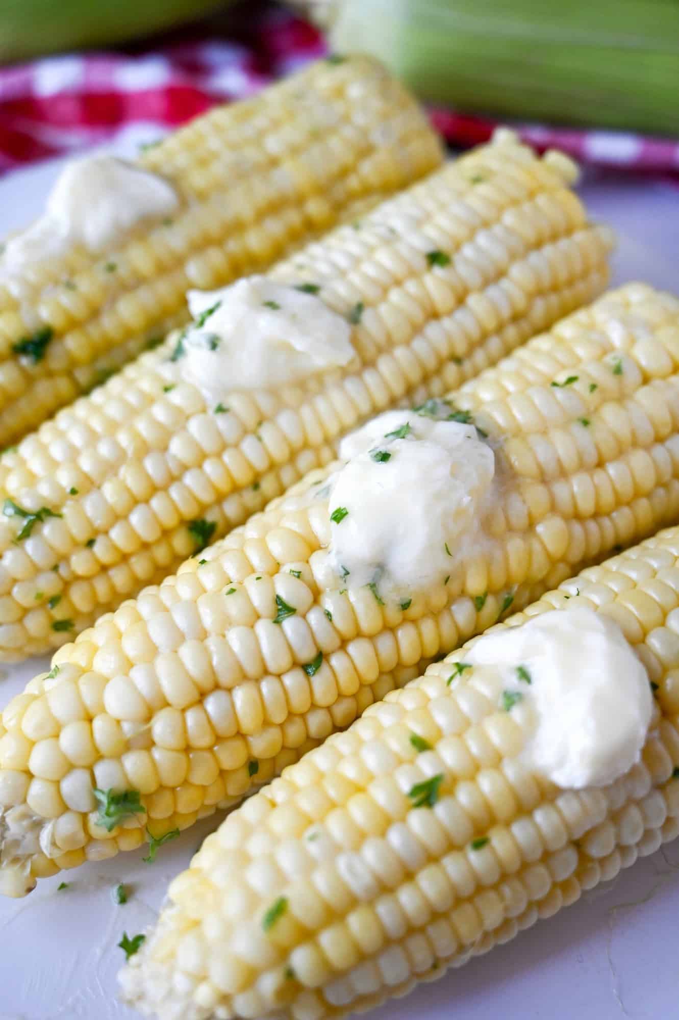 Microwave corn on the cob on a white plate with dabs of butter on each one.