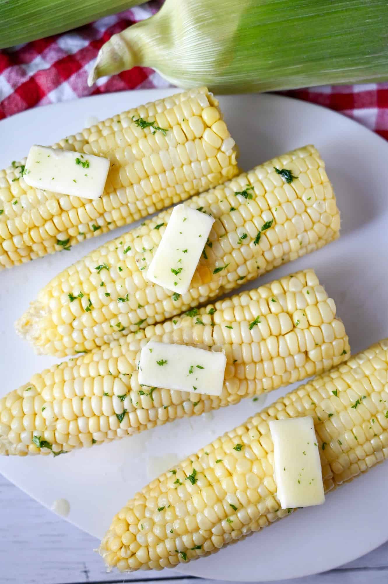 Four ears of microwaved corn on the cob and removed from the husk. Placed on a white plate with dabs of butter on each one.