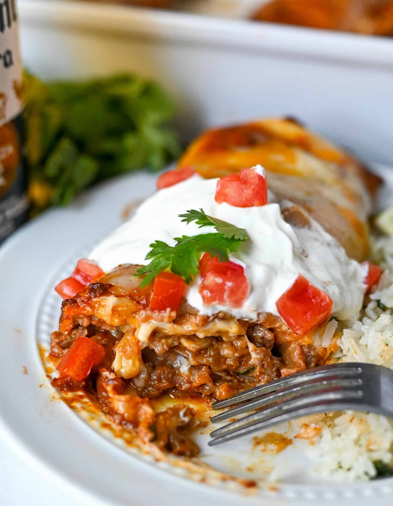 beef burrito on a white plate with sourcream on top and diced tomatoes. the end cut off and gooey, cheesy beef is oozing out. 