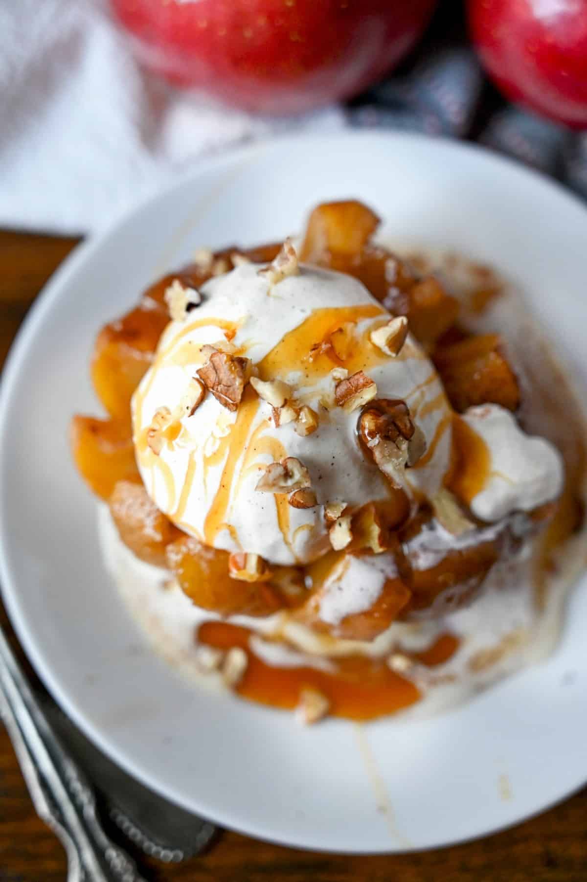 Bloomin grilled apple on a white plate with a scoop of ice cream, caramel sauce and pecans on top.