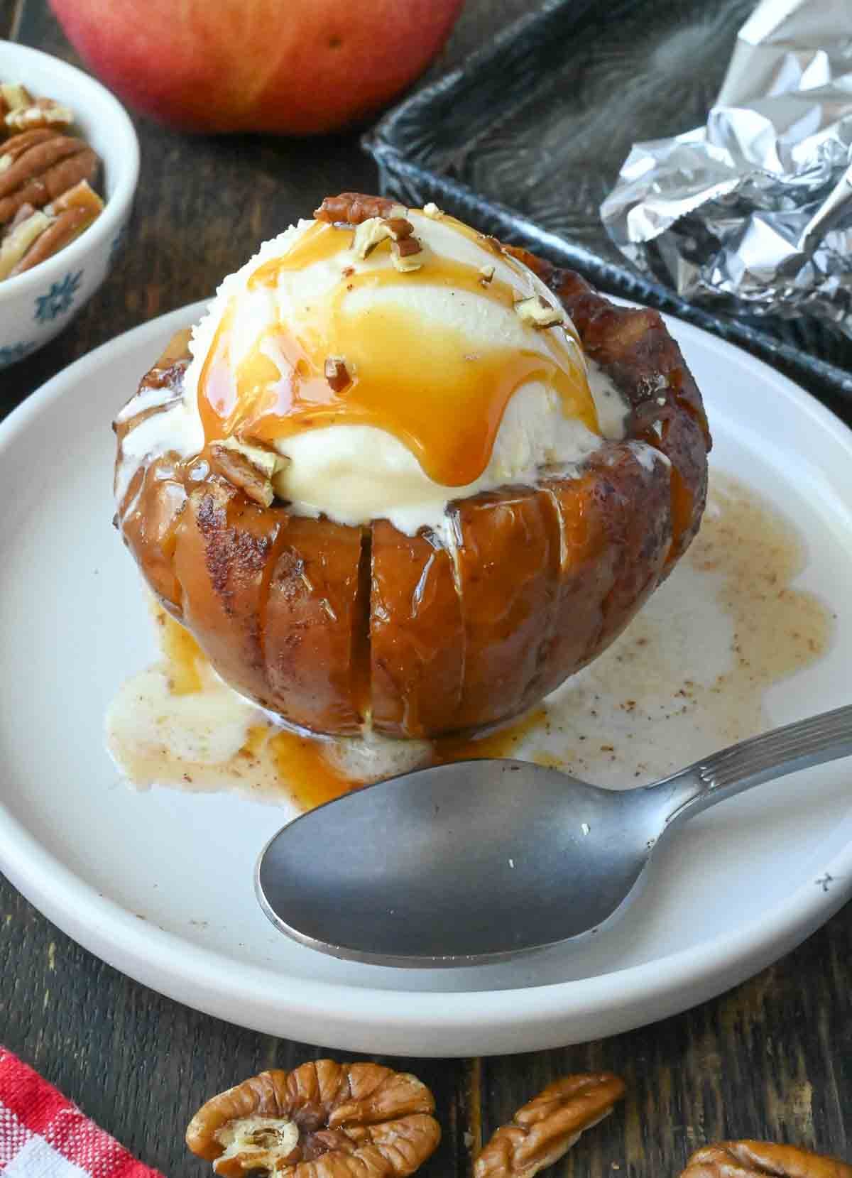 Grilled apple on a plate with a spoon and vanilla ice cream.