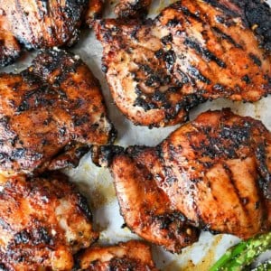 Sweet N Spicy grilled chicken thighs on a baking sheet with grilled asparagus and lemon slices.