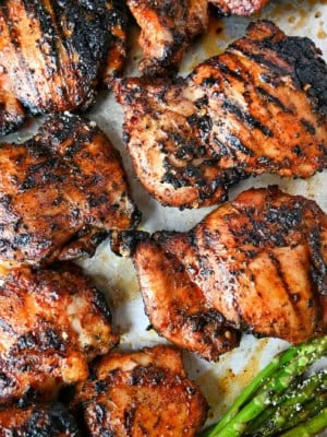 Sweet N Spicy grilled chicken thighs on a baking sheet with grilled asparagus and lemon slices.