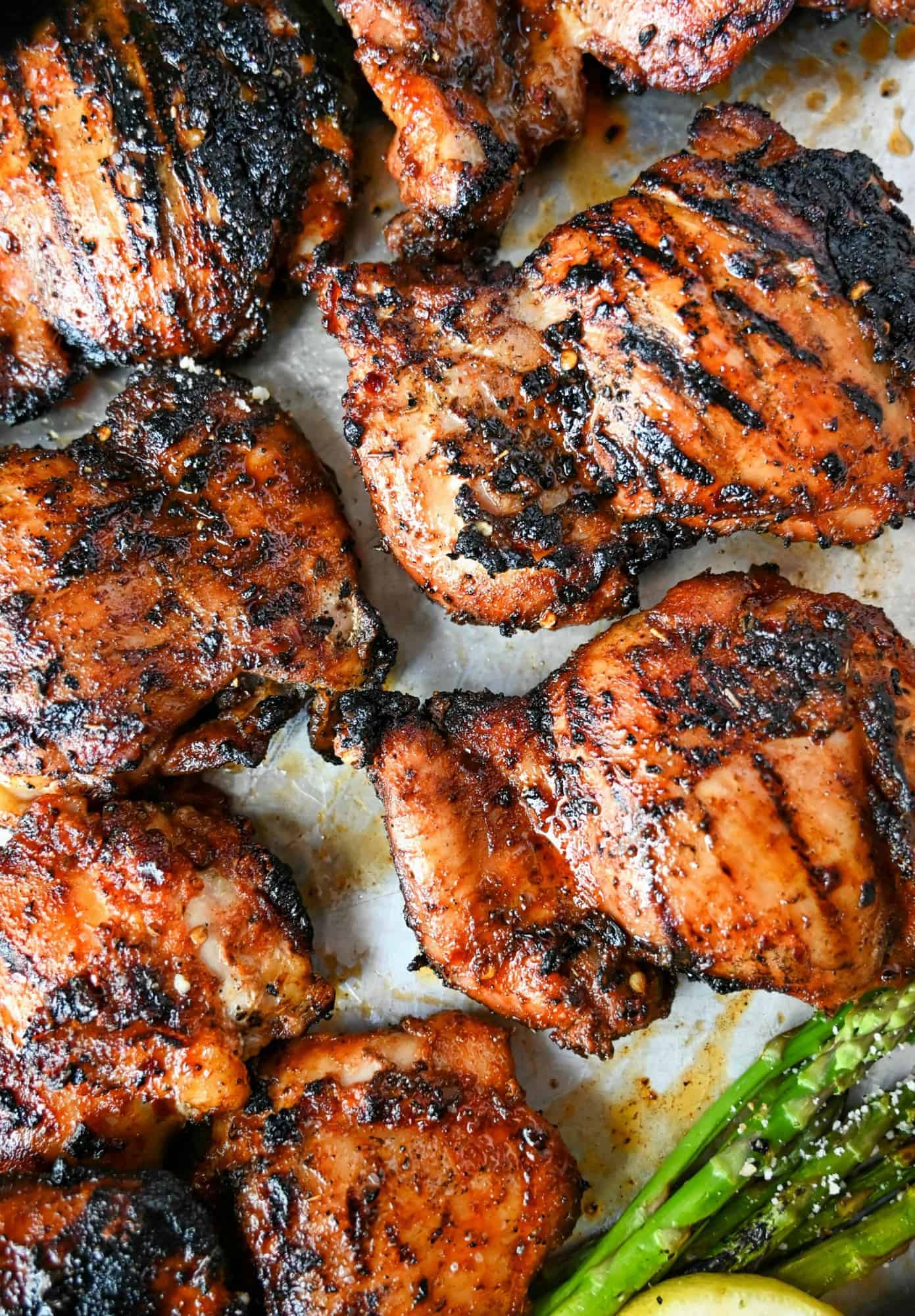 Sweet N Spicy grilled chicken thighs on a baking sheet with grilled asparagus and lemon slices.