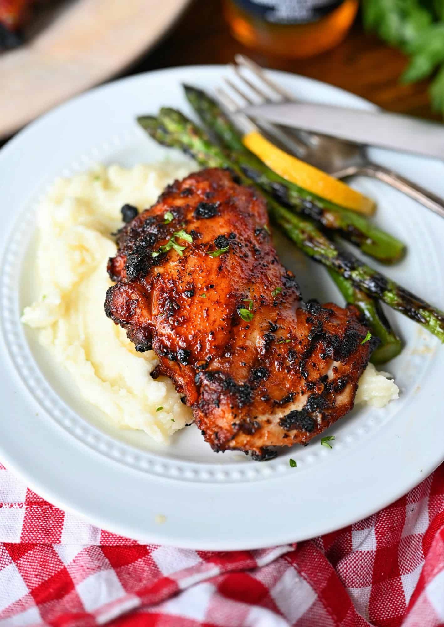 Sweet n spicy chicken on a white plate with mashed potatoes and grilled asparagus and a lemon slice.
