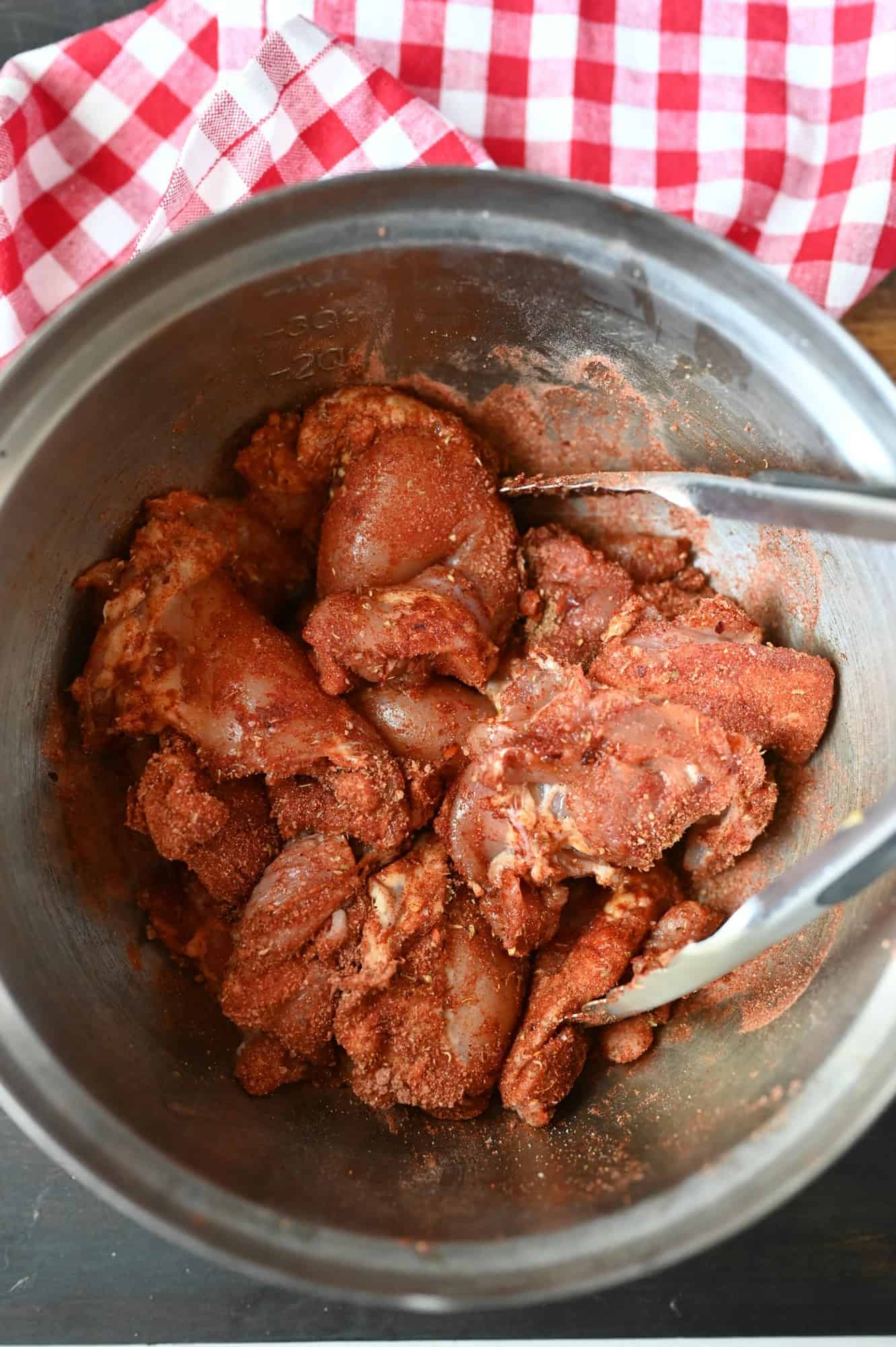 Raw chicken with spices sprinkled on in a metal bowl.