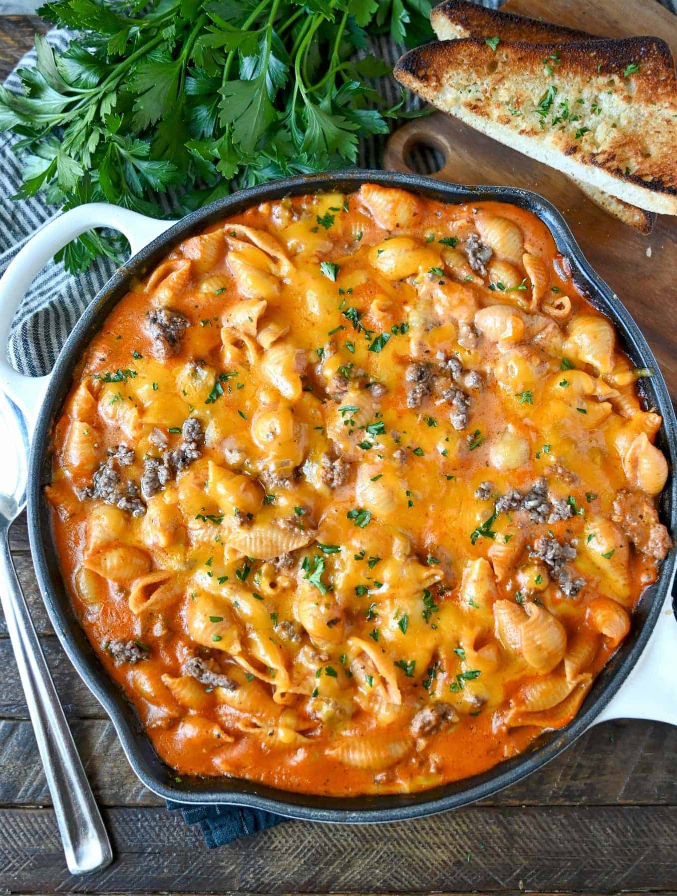 Creamy beef and shells with cheddar cheese on top in a cast iron skillet.