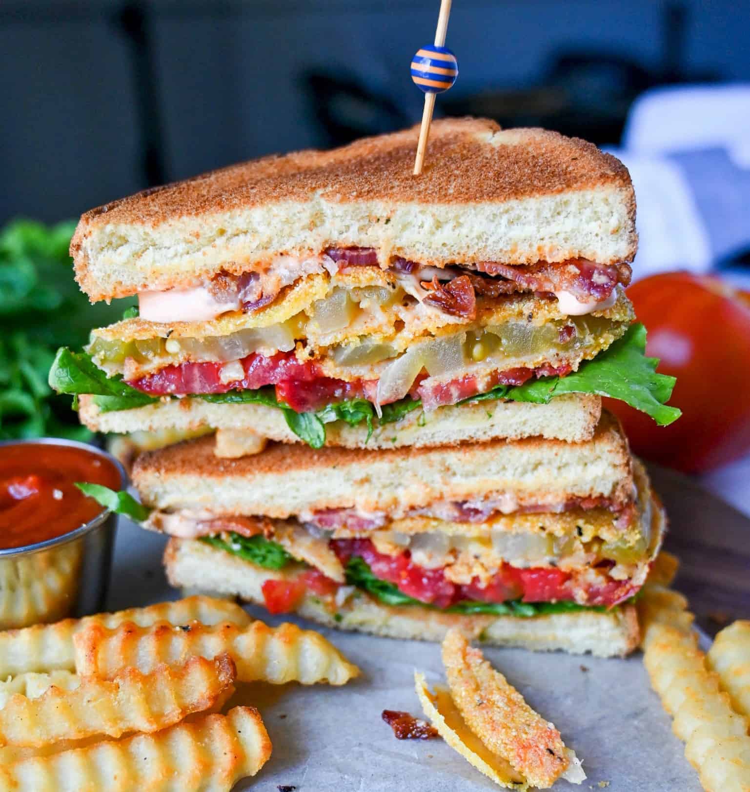 Fried green tomato sandwich cut in half and stacked on top of each other. With french fries and ketchup on the side.