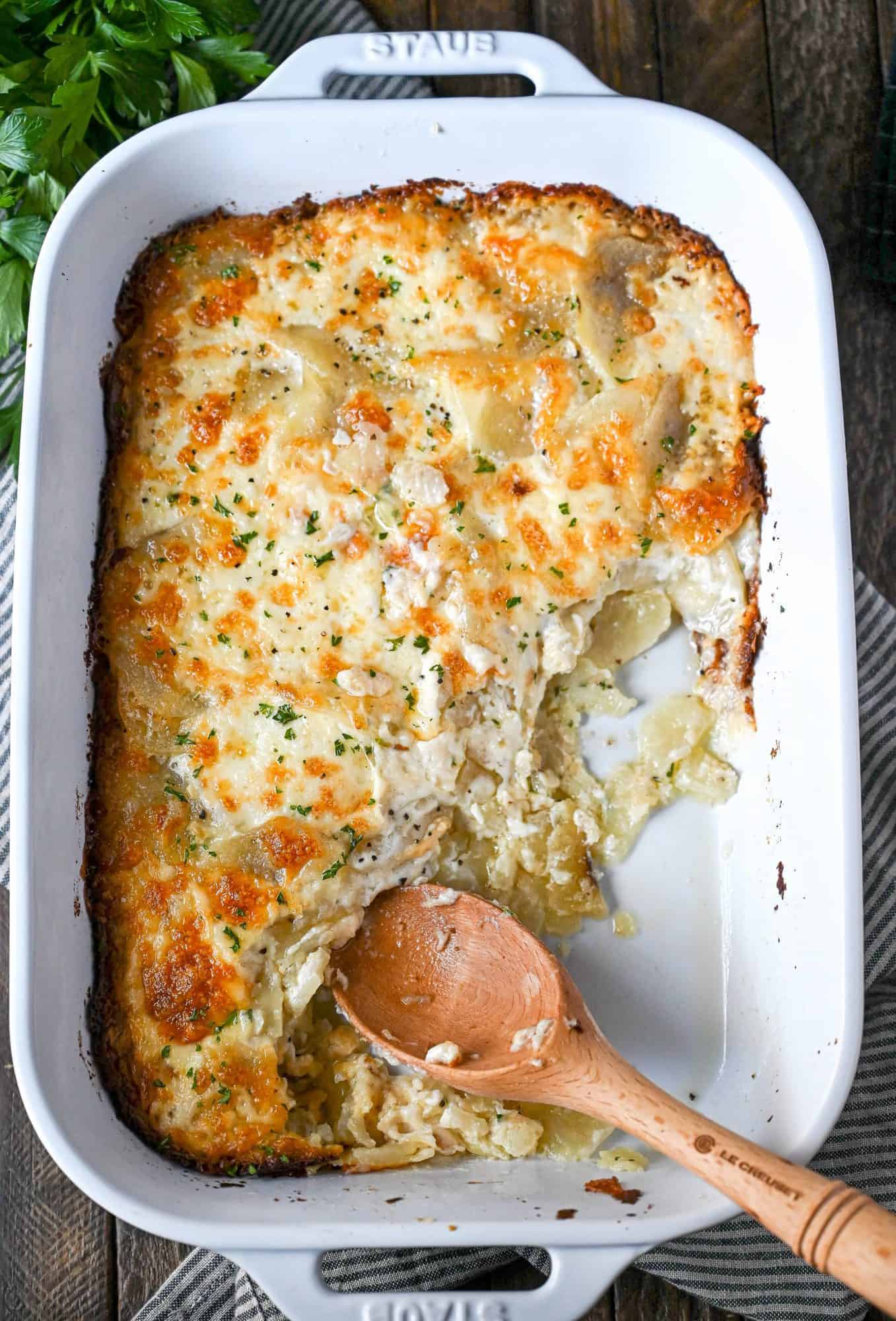 Potatoes au gratin in a white casserole dish with a few scoops missing.