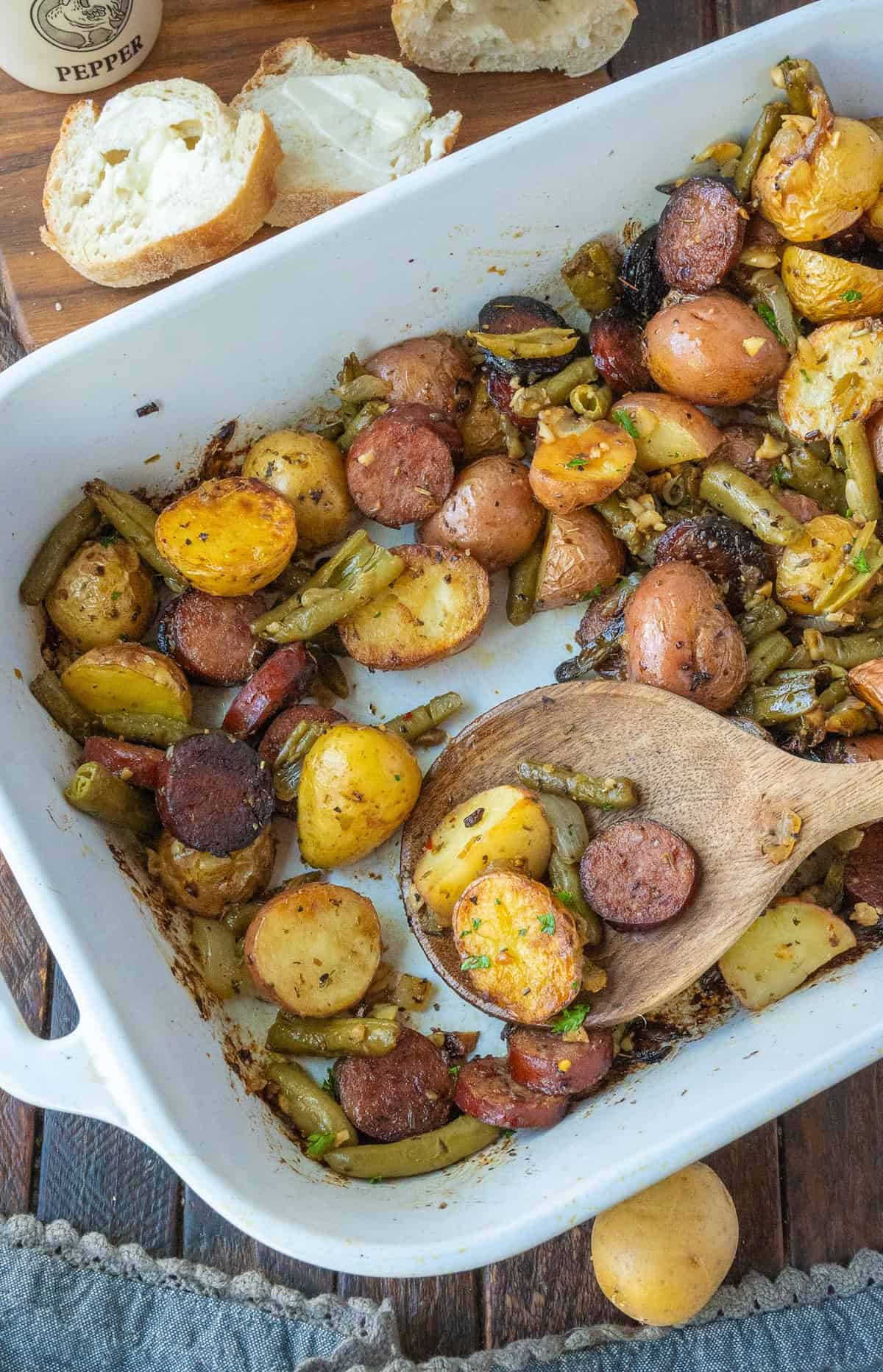 Sausage potato bake in a baking dish with a wooden spoon.