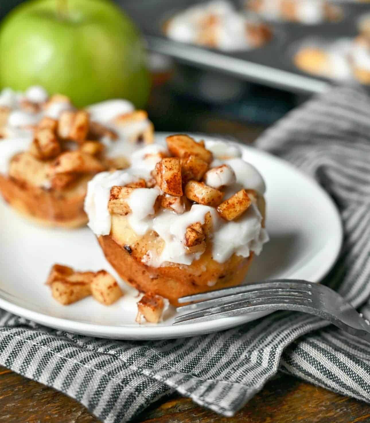 Cinnamon rolls with apples on top and icing on a white plate.