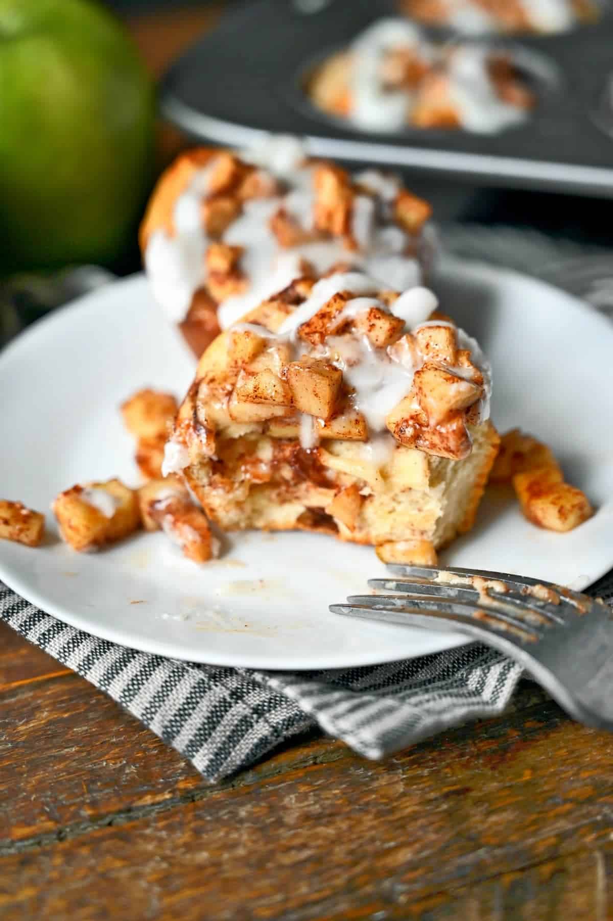 Apple pie cinnamon roll on a white plate and a fork that cut a piece out. 