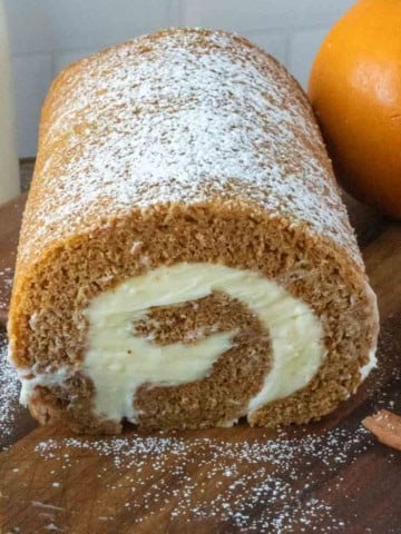 Pumpkin roll cake on a cutting board with powdered sugar on top.