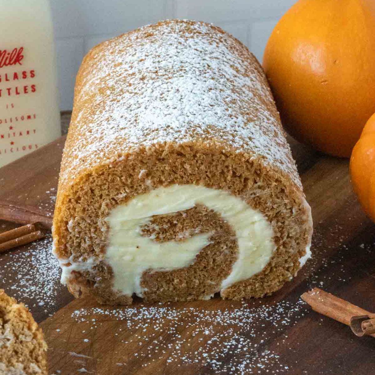 Pumpkin roll cake on a cutting board with powdered sugar on top.