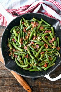 Green beans and bacon all in a skillet with a wooden spoon on the side.