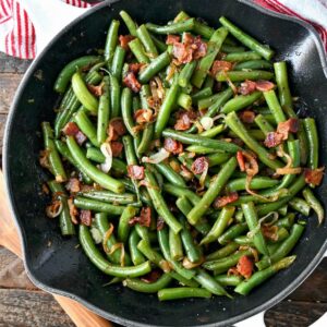 Green beans and bacon all in a skillet with a wooden spoon on the side.